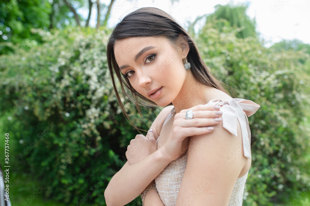 Young beautiful fashionable girl wearing stylish jewelry earrings and ring. Model poses on a street with blooming trees. Spring fashion concept. Young beautiful fashionable girl wearing stylish jewelry earrings and ring. Model poses on a street with blooming trees. Spring fashion concept.