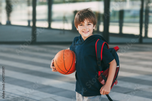 Portrait of a beautiful boy in sports uniform with a backpack and a basketball. The boy smiles and holds the ball in his hands. Training, education, physical education