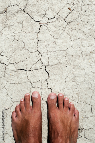 bare feet of a man on a cracked dry soil