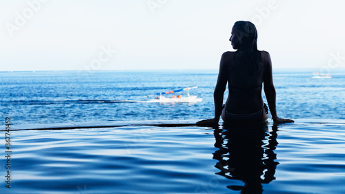 Woman at edge of infinity swimming pool with sea view.