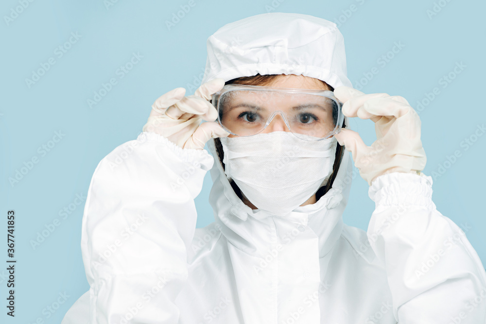 Fully geared up doctor in a white costume covering all skin, wearing mask, gloves and glasses. Prepared for virus outbreak. Adjusting glasses, serious face expression. Fully geared up doctor in a white costume covering all skin, wearing mask, gloves and glasses. Prepared for virus outbreak. Adjusting glasses, serious face expression.