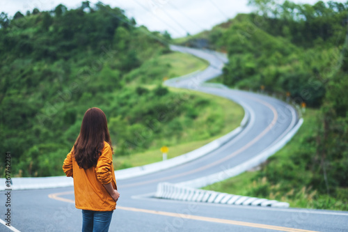 Rear view image of a young female traveler with curved and winding asphalt road in high mountains