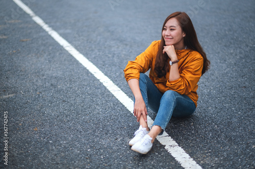 Portrait image of a beautiful young asian female traveler sitting on an asphalt road