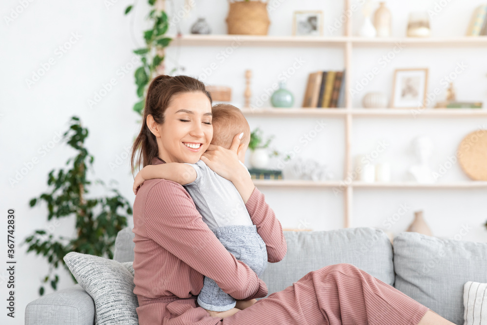 Mother-Child Connection. Happy Mom Hugging Her Toddler Baby While Relaxing On Couch Mother-Child Connection. Happy Mom Hugging Her Toddler Baby While Relaxing On Couch