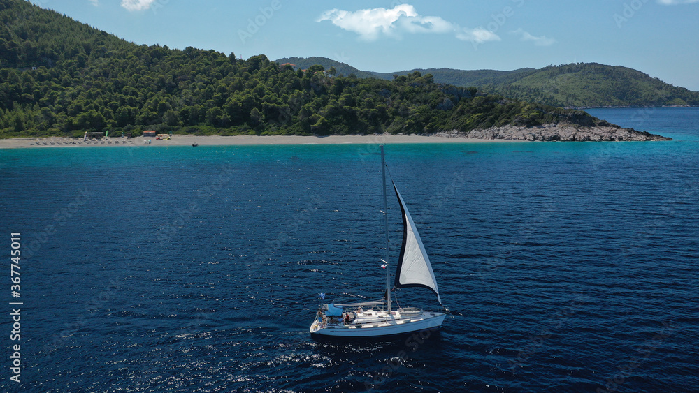 Aerial drone photo of sailing boat cruising near famous turquoise paradise beach of Milia covered with pine trees, Skopelos island, Sporades, Greece Aerial drone photo of sailing boat cruising near famous turquoise paradise beach of Milia covered with pine trees, Skopelos island, Sporades, Greece