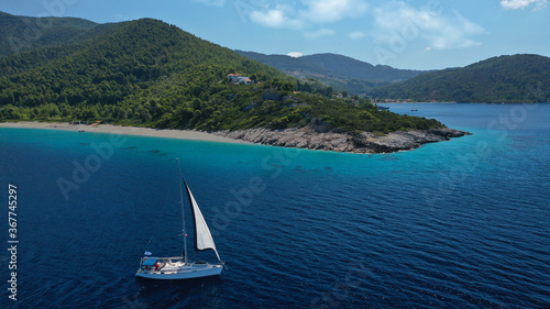 Aerial drone photo of sailing boat cruising near famous turquoise paradise beach of Milia covered with pine trees, Skopelos island, Sporades, Greece