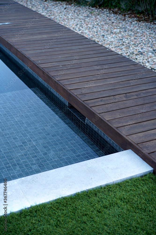 Blue swimming pool with wooden deck                       