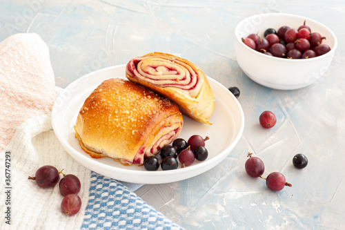 Fresh buns with berry filling decorated with black currants and gooseberry on a light blue concrete background.