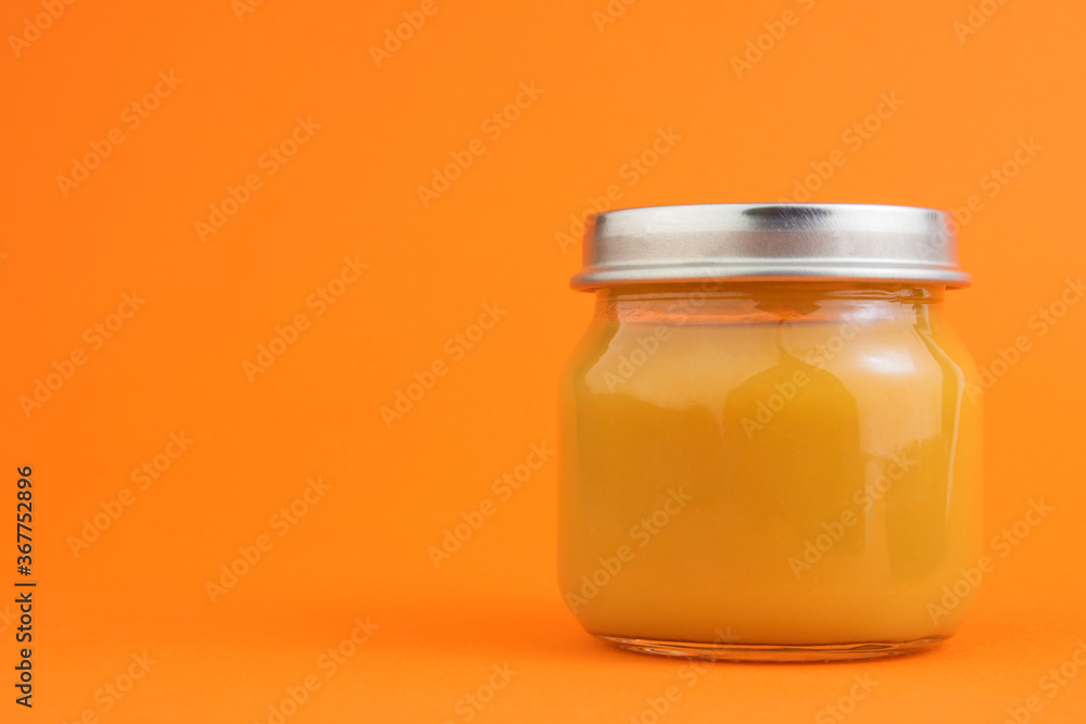 Canned vegetable or fruit puree in a glass jar on an orange background. The concept of baby food, canned food, orange vegetables or fruits. Copy space Canned vegetable or fruit puree in a glass jar on an orange background. The concept of baby food, canned food, orange vegetables or fruits. Copy space