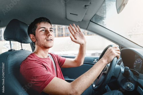 Joyful and careless car driver raises his hand in thanks for giving way. Traffic rules and politeness concept