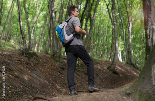 Adult man hiking through the green forest, in summer