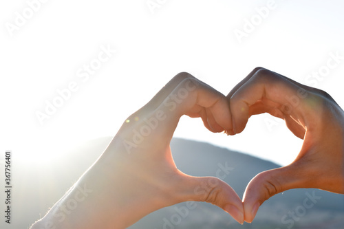 hands folded in the shape of a heart against the background of mountains and sky