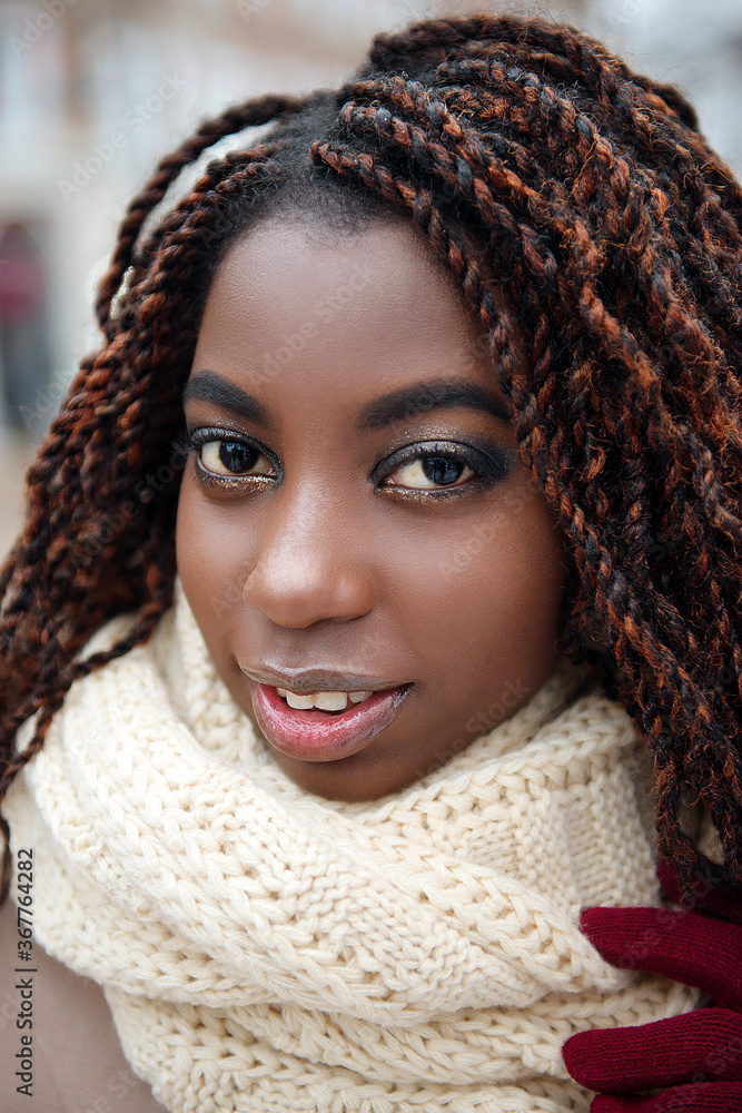 African girl smiling with makeup and in a beige scarf, close-up in a winter day. African girl smiling with makeup and in a beige scarf, close-up in a winter day.
