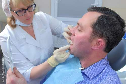 Dentist woman is teaching patient man to clean teeth using dental floss in dentistry. Stomatologist cleaning man teeth with dental floss in stomatology  side view. Hygiene and health of oral cavity.