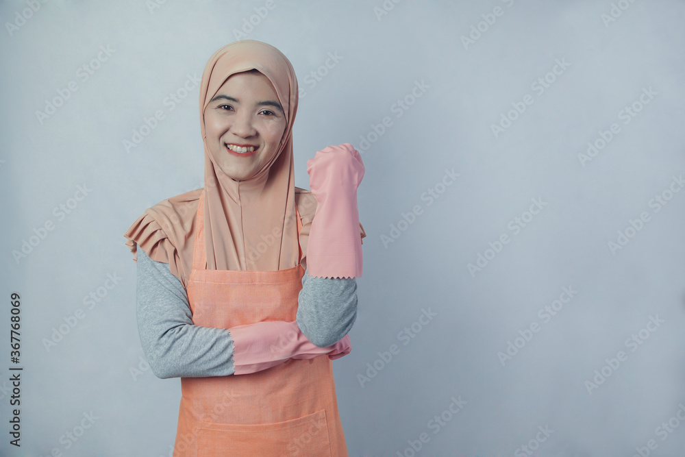 Fototapeta premium Young muslim woman housewife with pink rubber gloves in apron on grey background