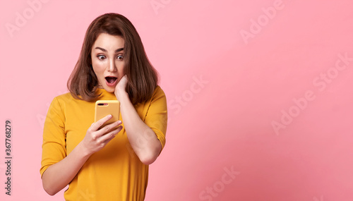 happy and surprise young woman good looking using mobile phone on pink copy space background. photo