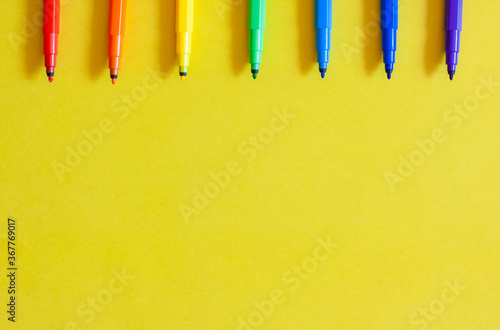 Markers of rainbow colors on a yellow background  top view  copy space