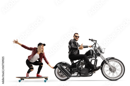 Female riding a skateboard and holding onto a chopper motorbike