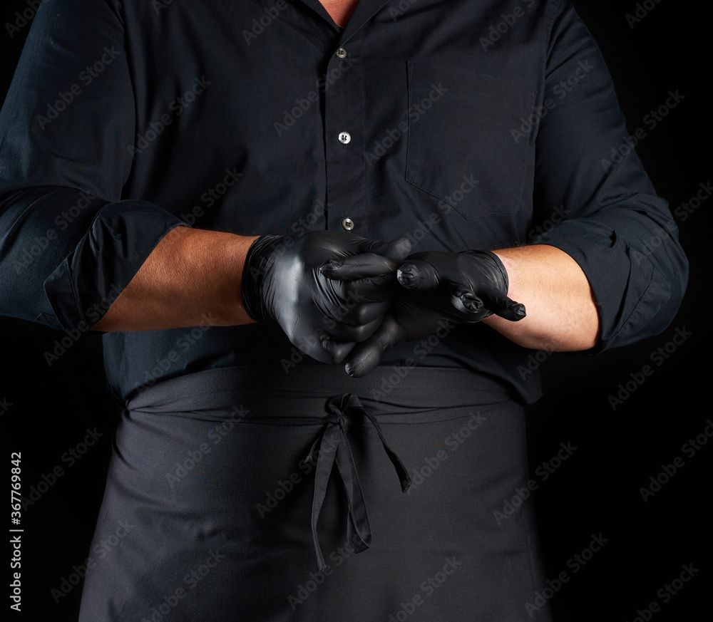 chef in black shirt and apron puts black latex gloves on his hands before preparing food