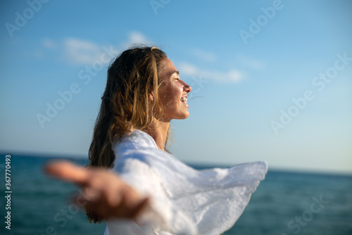 Authentic close up shot of an young carefree woman tourist is feeling free and breathing deeply with wide arms open on scenic seascape during holidays vacation trip. photo