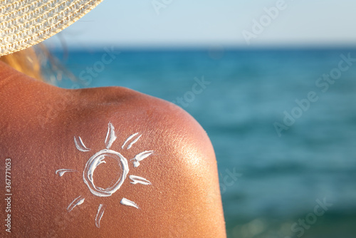 Close up of an young woman with applied sun shape of sunscreen or sun tanning lotion on a shoulder to take care of her skin on a seaside beach during holidays vacation.