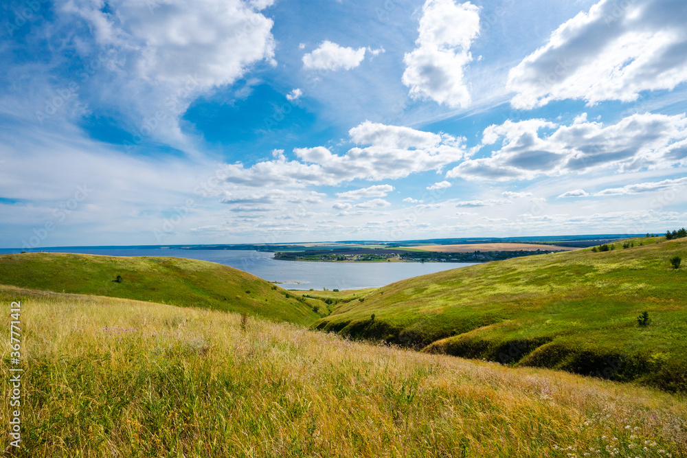 Panorama of the Russian picturesque landscape with hills and flower fields and blue sky with clouds on the background of the sea