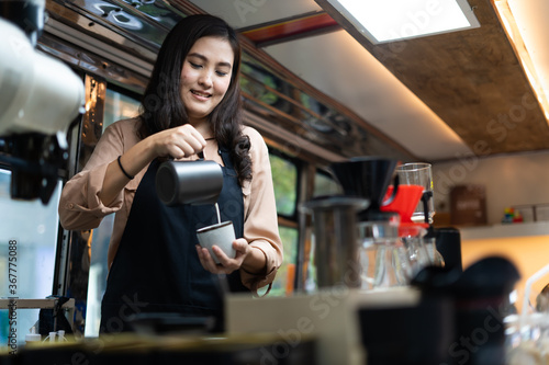 Young Asian woman pouring milk into coffee making late coffee. Professional barista preparing coffee on counter