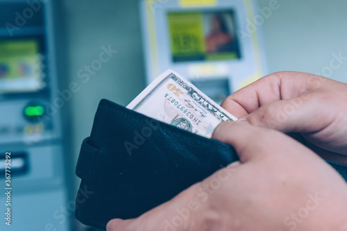 A man holds a wallet with dollars in his hands on the background of an ATM.