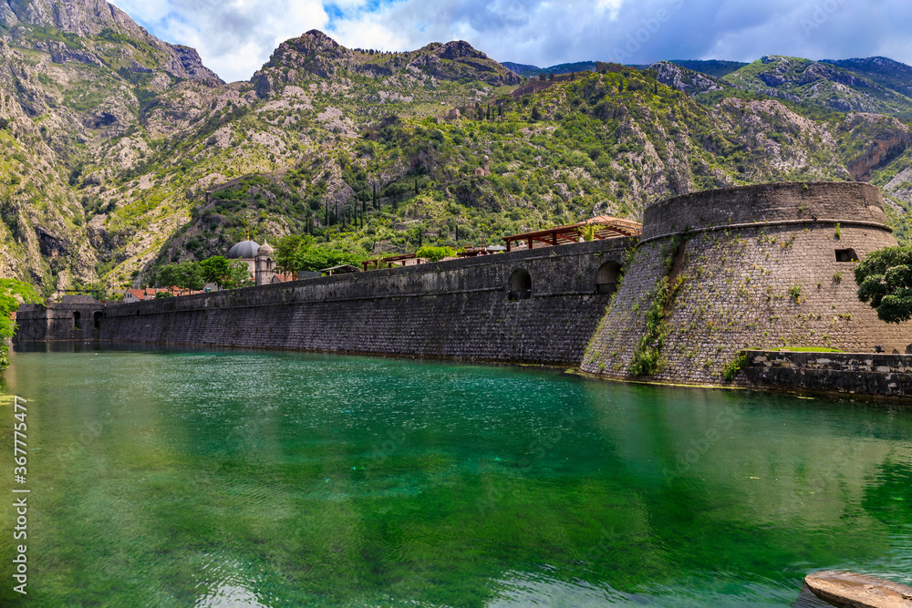Emerald green waters of Kotor Bay or Boka Kotorska, mountains and the ancient stone city wall of Kotor old town former Venetian fortress in Montenegro