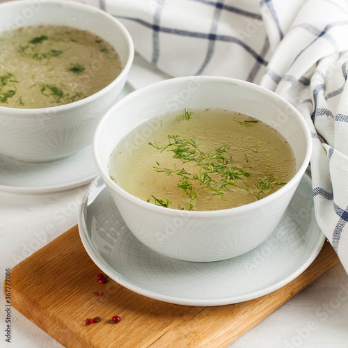 Homemade chicken broth in a white bowl on a wooden background. The concept of healthy eating. Copy space.