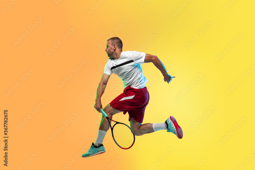 One caucasian man playing tennis isolated on studio background in neon light. Fit young professional male player in motion or action during sport game. Concept of movement, sport, healthy lifestyle. One caucasian man playing tennis isolated on studio background in neon light. Fit young professional male player in motion or action during sport game. Concept of movement, sport, healthy lifestyle.
