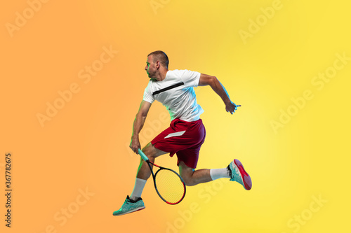 One caucasian man playing tennis isolated on studio background in neon light. Fit young professional male player in motion or action during sport game. Concept of movement, sport, healthy lifestyle.