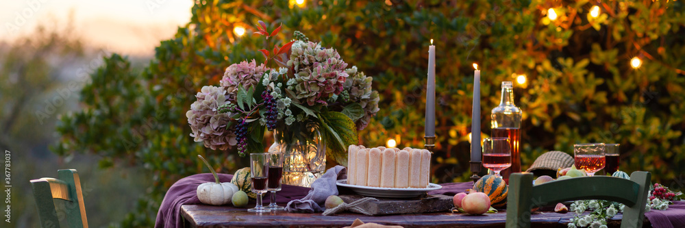 Beautiful and elegant table setting for a romantic date for a couple. Delicious meal, tasty dessert. Private terrace outside the restaurant. Lights on the tree on background. Italy, Tuscany. Banner
