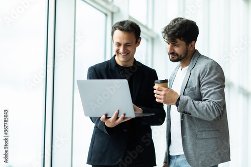 Two cheerful businessmen discussing something on the laptop in an office