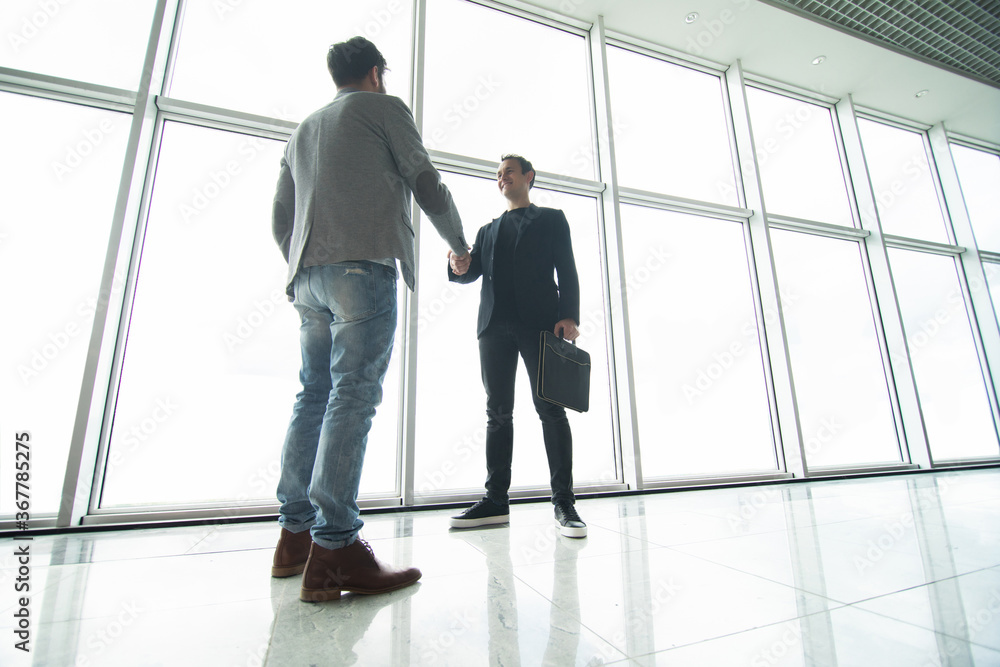 Two businessmen handshake in modern office with big panoramic windows Two businessmen handshake in modern office with big panoramic windows