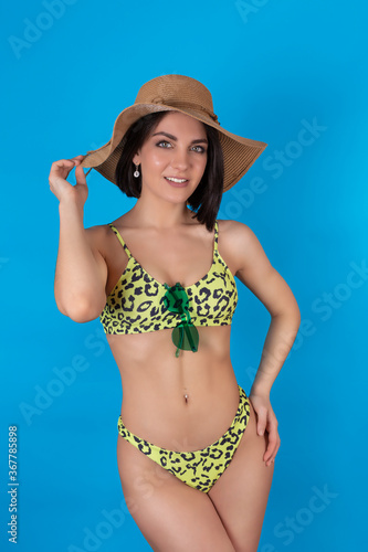 Portrait of a happy cheerful woman in a summer hat, leopard print swimsuit, isolated on a blue background. The concept of leisure and travel