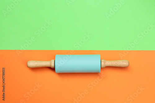 Small rolling pin in blue color on green and orange background. kitchen tool