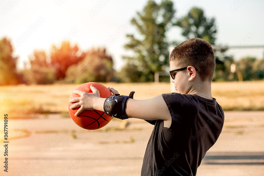 A teenage boy basketball player focused and pulled an orange basketball in his hands to the side of the ring, prepared to throw. Training and sports. Active lifestyle of children