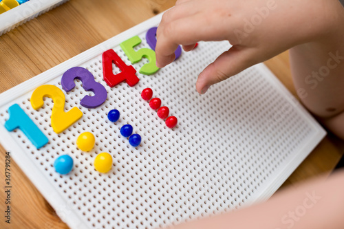 By provided numbers boy inserting pins. counting game. mathematical task. play at home. way of learning.