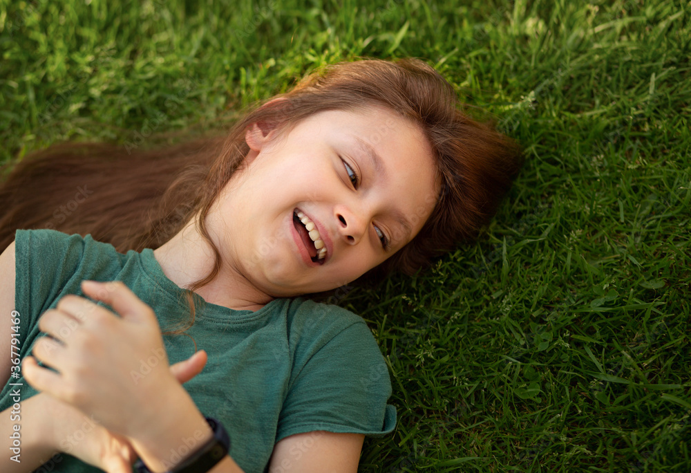Laughing playful kid girl lying on the grass on nature summer background. Closeup positive outdoors bright sunny Laughing playful kid girl lying on the grass on nature summer background. Closeup positive outdoors bright sunny