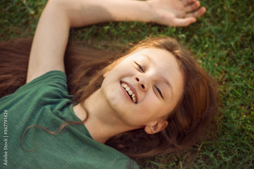 Laughing playful kid girl lying on the grass on nature summer background. Closeup positive outdoors bright sunny Laughing playful kid girl lying on the grass on nature summer background. Closeup positive outdoors bright sunny