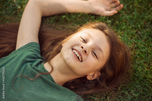 Laughing playful kid girl lying on the grass on nature summer background. Closeup positive outdoors bright sunny