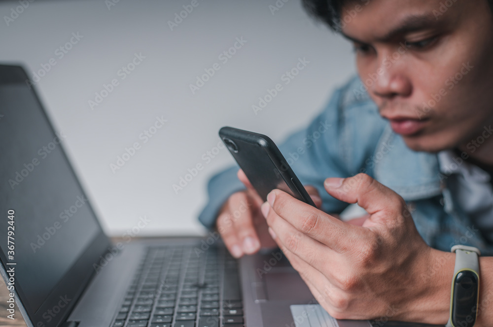 Men use their smartphones while resting from work, tired from work. Relax in front of the notebook computer on the desk. Men use their smartphones while resting from work, tired from work. Relax in front of the notebook computer on the desk.