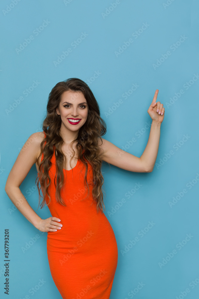 Beautiful Smiling Woman In Orange Dress Is Pointing Up