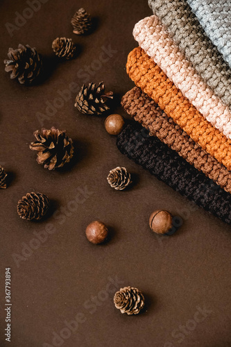 Stack of knitted material from threads of brown, orange, gray colors with pine cones a brown background. Top view. Copy, empty space for text