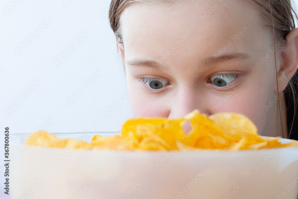 A teenage girl looks with wild, wide-open eyes at a bowl full of chips, face close-up A teenage girl looks with wild, wide-open eyes at a bowl full of chips, face close-up