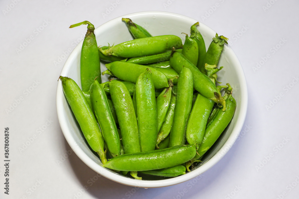 Peas in a pod. Freshly picked sugar snap peas in a bowl. The vibrant green pea pods are set against a white background. These high fiber, low calorie vegetables are ideal for a healthy snack. Peas in a pod. Freshly picked sugar snap peas in a bowl. The vibrant green pea pods are set against a white background. These high fiber, low calorie vegetables are ideal for a healthy snack.