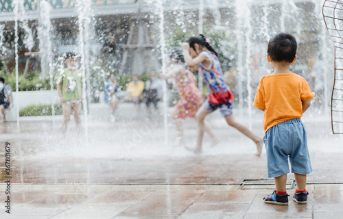 An adorable toddler Asian boy (1-year-old) standing and enjoy to see outdoor public fountains a water splashing for the first time
