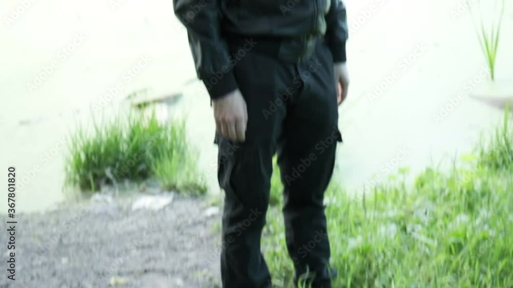 man in gas mask, black leather jacket with hood standing outdoors at forest near lake. protection from chemical weapons, virus epidemic. Post apocalyptic world. survivor, stalker after nuclear war man in gas mask, black leather jacket with hood standing outdoors at forest near lake. protection from chemical weapons, virus epidemic. Post apocalyptic world. survivor, stalker after nuclear war