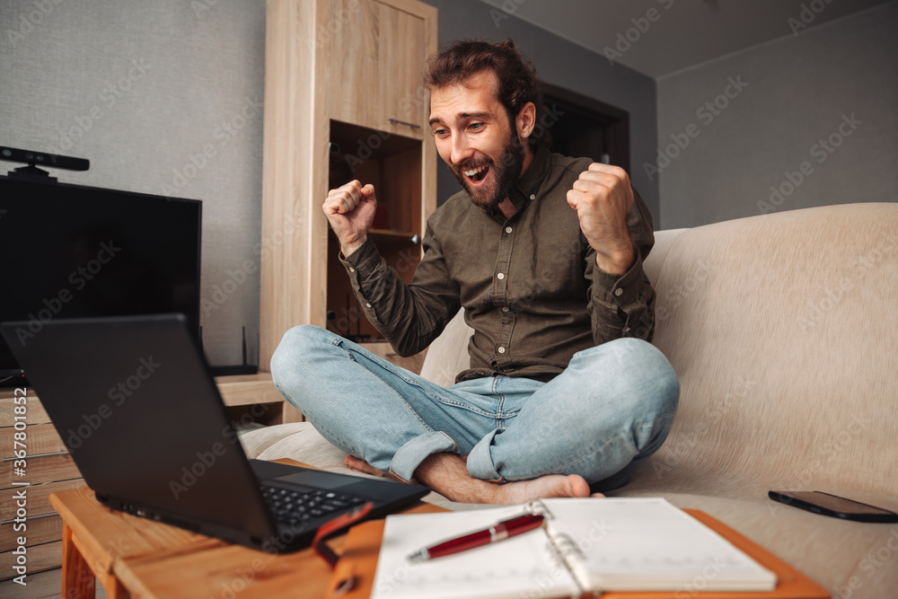 Portrait of a happy man working at home using a laptop, the guy rejoices and shouts with delight Portrait of a happy man working at home using a laptop, the guy rejoices and shouts with delight